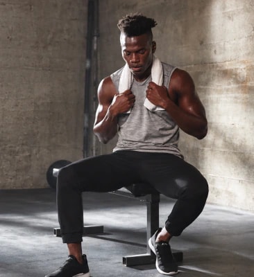 Man resting on a weight bench with a towel around his neck in a concrete gym